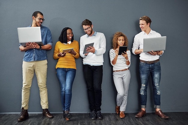 La tecnología inalámbrica funciona en cualquier lugar Toma completa de un grupo de empresarios que usan tabletas y computadoras portátiles mientras esperan en la fila para una entrevista de trabajo