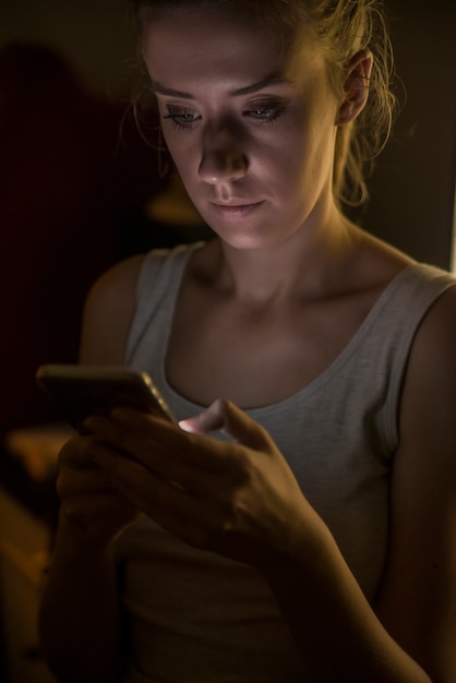 Foto tecnologia, internet, comunicação e conceito de pessoas - mensagens de mulher jovem em smartphone em casa à noite