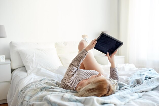 tecnologia, internet e conceito de pessoas - jovem feliz deitada na cama com computador tablet pc no quarto de casa