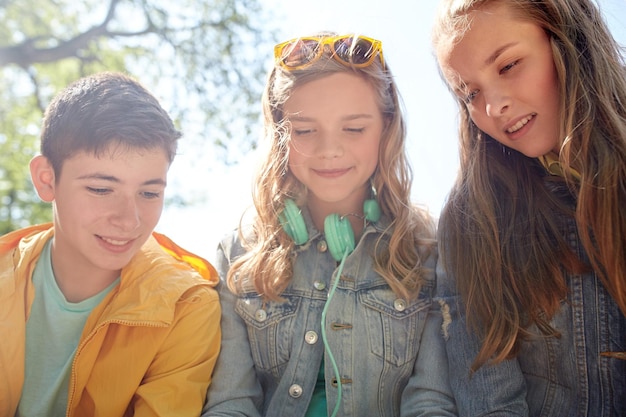 tecnologia, internet e conceito de pessoas - três amigos adolescentes felizes com fones de ouvido ao ar livre olhando para algo