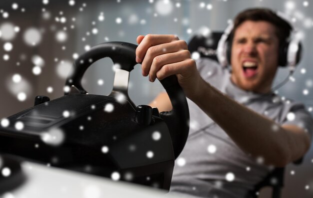 Tecnologia, jogos, entretenimento, vamos jogar e conceito de pessoas - jovem zangado em fones de ouvido com computador pc jogando videogame de corrida de carros em casa e volante sobre a neve