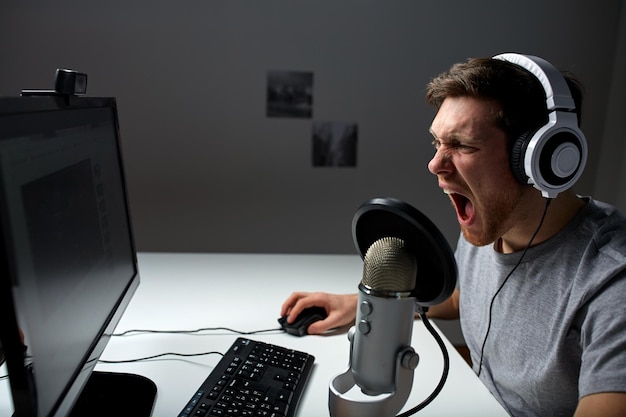 tecnología, juegos, entretenimiento, juguemos y el concepto de la gente: un joven enojado que grita con auriculares con una computadora de PC jugando en casa y transmitiendo videos de reproducción o tutoriales