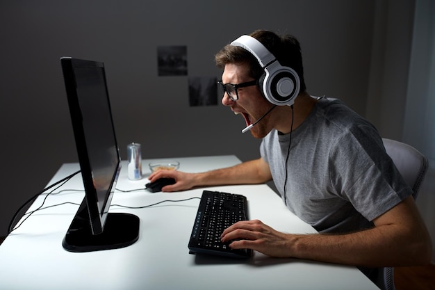 tecnología, juegos, entretenimiento, juguemos y el concepto de la gente: un joven enojado que grita con auriculares con una computadora de PC jugando en casa y transmitiendo videos de reproducción o tutoriales