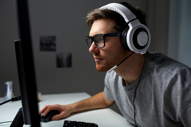 tecnología, juegos, entretenimiento, juguemos y concepto de personas: joven con auriculares y anteojos con computadora de PC jugando en casa y transmitiendo videos de recorrido o recorrido