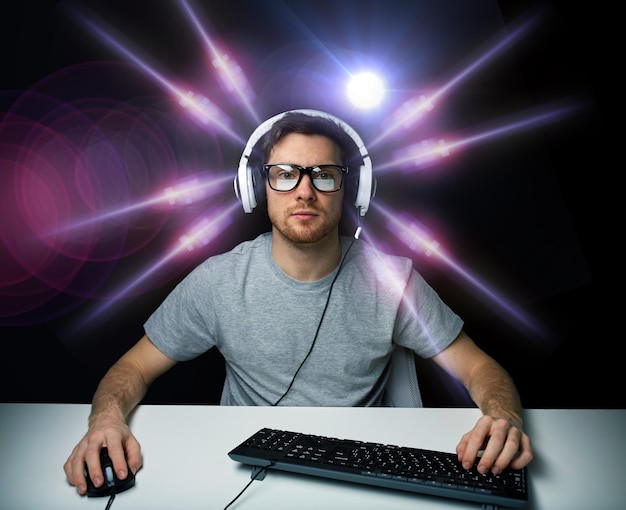 tecnología, juegos, entretenimiento, juguemos y concepto de personas: joven con auriculares y anteojos con computadora de PC jugando y transmitiendo reproducción o video de recorrido sobre luz