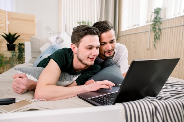 Tecnología moderna. Bastante joven pareja gay usando laptop mientras posa en la cama y pasar tiempo juntos