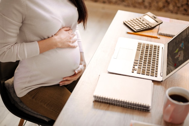 Tecnologia moderna. Close-up de jovens mãos femininas colocadas na barriga enquanto a mulher está sentada na cadeira e fazendo uma pausa