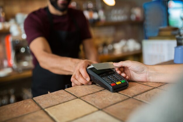 Foto tecnología moderna y concepto de personas - hombre o camarero con terminal de pago y mano de cliente con tarjeta de crédito en el bar de la cafetería