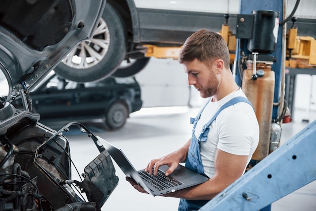 Tecnología moderna. Empleado con uniforme de color azul trabaja en el salón del automóvil.