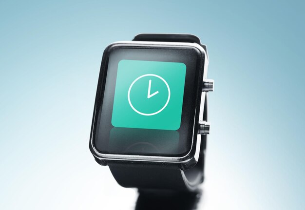 tecnología moderna, tiempo, objeto y concepto de medios - cierre de reloj inteligente negro con icono de reloj en pantalla sobre fondo azul
