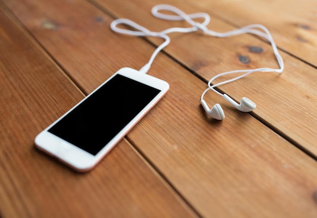 tecnologia, música, gadget e conceito de objeto - close-up de smartphone branco e fones de ouvido na superfície de madeira com espaço de cópia