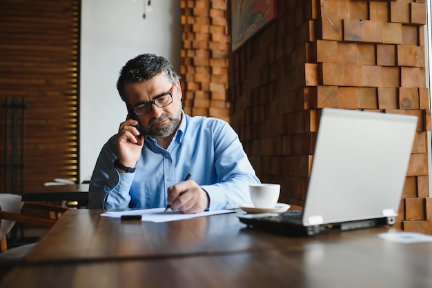 Tecnología de negocios y concepto de personas empresario senior con computadora portátil tomando café en un café moderno