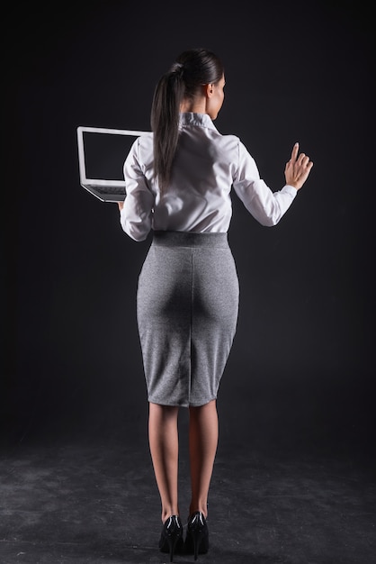 Tecnologia nos negócios. Mulher de negócios atraente e profissional segurando um laptop e olhando para o dedo enquanto usa tecnologia moderna para seu trabalho