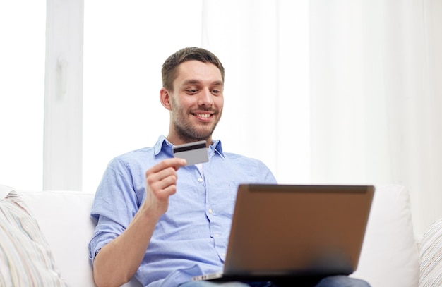 tecnología, personas y concepto de compras en línea - hombre sonriente con laptop y tarjeta de crédito en casa