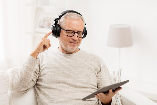 tecnología, personas, estilo de vida y concepto de aprendizaje a distancia - feliz anciano con tablet pc y auriculares escuchando música en casa