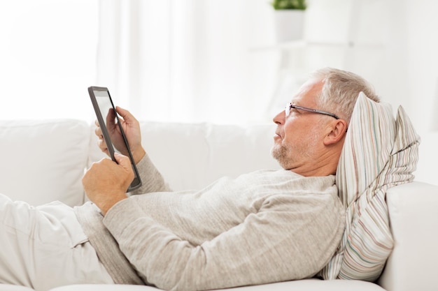 tecnología, personas y estilo de vida, concepto de aprendizaje a distancia - hombre mayor con computadora de tablet pc acostado en el sofá en casa