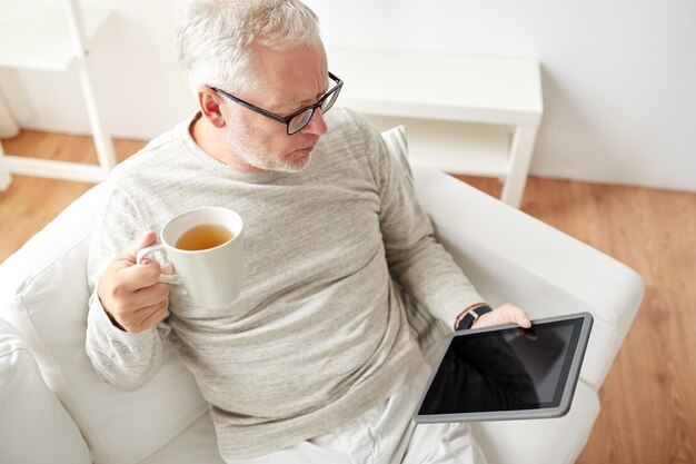 tecnologia, pessoas e conceito de estilo de vida - homem sênior com computador tablet pc bebendo chá em casa