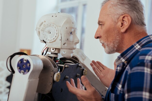 Tecnología progresiva. Ingeniero inteligente serio mirando al robot mientras está parado frente a él