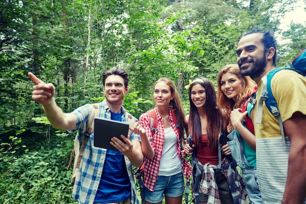 tecnologia, viagens, turismo, caminhada e conceito de pessoas - grupo de amigos sorridentes andando com mochilas e computador tablet pc procurando localização na floresta