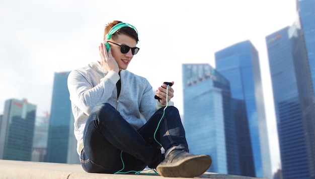 tecnologia, viagens, turismo e conceito de pessoas - sorridente jovem ou adolescente em fones de ouvido com smartphone ouvindo música sobre fundo de arranha-céus da cidade de singapura