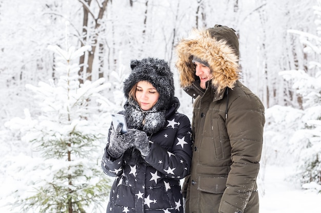 Tecnologías y concepto de relación - Feliz pareja sonriente tomando un selfie en un bosque de invierno afuera.