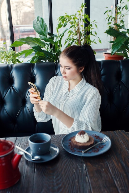 Tecnologías emociones estilo de vida personas adolescentes concepto Joven mujer feliz leyendo en su teléfono móvil mientras está sentada en el interior de la cafetería moderna chica con una hermosa sonrisa bebe té