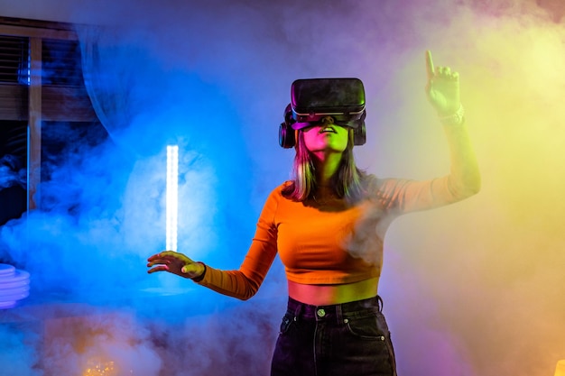 Tecnologías inalámbricas Mujer joven con gafas de realidad virtual en la habitación oscura con iluminación de neón