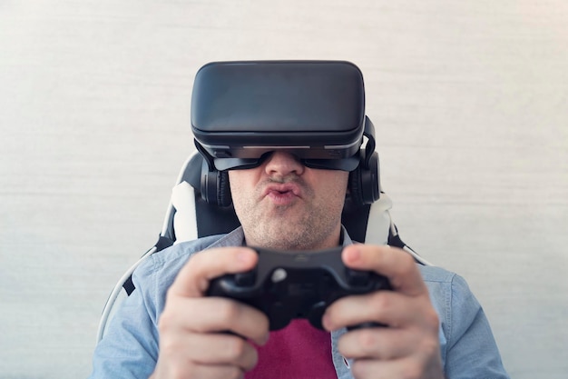 Tecnologías modernas y concepto de entretenimiento doméstico Joven probando la realidad virtual en casa usando auriculares VR y sosteniendo joystick jugando videojuegos