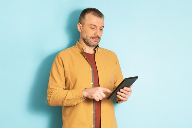 Tecnologias modernas Homem de meia-idade confiante segurando e usando tablet digital em pé sobre o fundo azul do estúdio