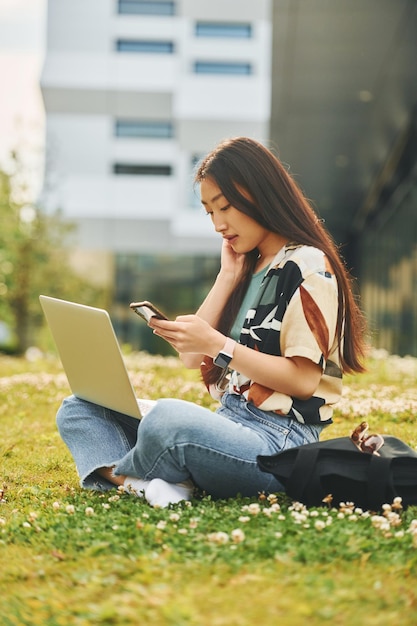 Tecnologias sem fio A jovem asiática está ao ar livre durante o dia