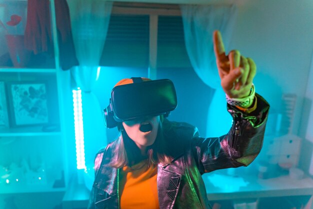 Tecnologias sem fios Mulher jovem usando óculos de realidade virtual na sala escura com iluminação de néon
