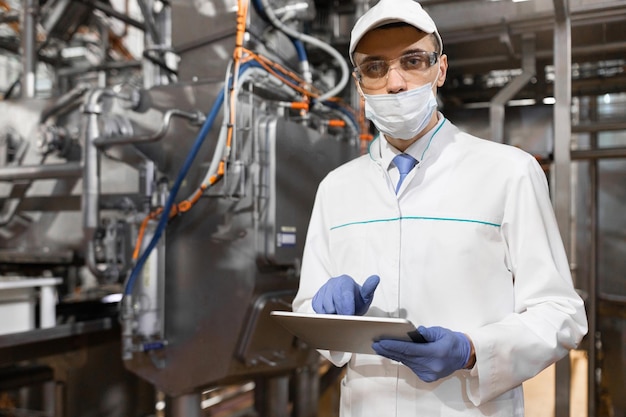 Foto un tecnólogo concentrado que toma las notas necesarias con la ayuda de una tableta digital mientras se encuentra en el departamento de producción del inspector de la fábrica de productos lácteos lleva a cabo el control en la fábrica de queso