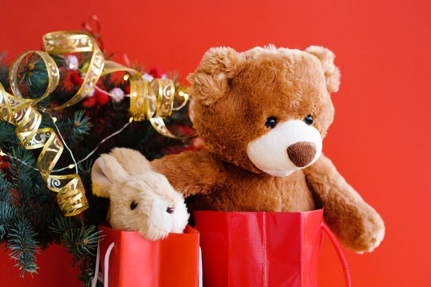 Teddy y conejito en bolsas de regalo rojo bajo el árbol de Navidad.