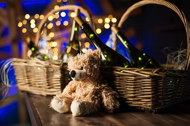 Teddybär-Champagnerflasche mit Weihnachtskorb-Goldgirlanden auf dunkelbraunem Holzhintergrund Neujahrsfeier conceptxA