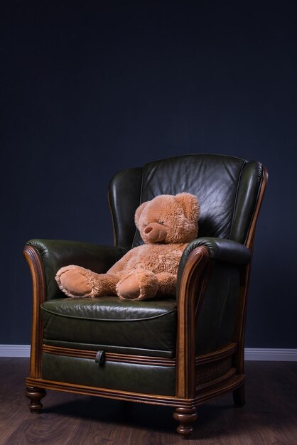 Teddybär sitzt in einem grünen Ledersessel vor der Wand