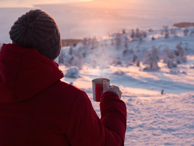 Tee bei einem frostigen Sonnenuntergang Mann mit einer Tasse Tee bei Sonnenaufgang Kaffee aus dem Freien Schneebedeckter Berghintergrund Winterurlaub Tourismus Reise- und Personenkonzept