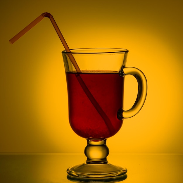 Tee-Cocktail-Fruchtgetränk in einer Glasschale mit einem Trinkhalm auf dem Tisch Rotes Getränk in einem Becher auf einem schönen leuchtend gelben Hintergrund mit Farbverlauf Sommergetränke-Konzept