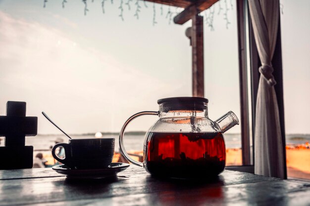 Tee in einer Teekanne aus Glas und einer Tasse auf einem Holztisch im Freien Café-Brunch an der Küste