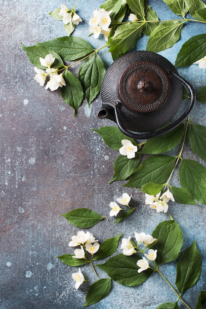 Tee Jasmin Hintergrund mit Teekanne, Blätter und Blumen auf dunkler Textur, Draufsicht, Kopienraum, vertikal