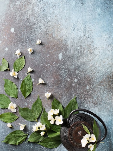 Tee Jasmin Hintergrund mit Teekanne, Blätter und Blumen auf dunkler Textur, Draufsicht, Kopienraum, vertikal