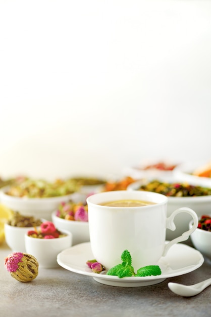 Tee-Konzept mit textfreiraum. Verschiedene trockene Teesorten in weißen Keramikschalen und eine Tasse aromatischen Tee