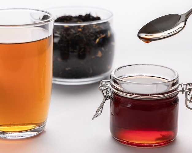 Tee-Konzept, schwarze Teeblätter, Teegetränk in der Glasschale und Honig im Glas auf dem Tisch, goldener Honig im Löffel