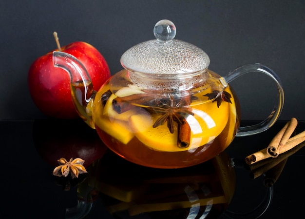 Tee mit Apfelzimt und Anis in der Glasteekanne auf dem dunklen Hintergrund Nahaufnahme