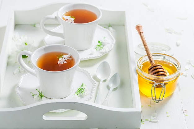 Tee mit Honig, serviert auf einem weißen, mit Blumen geschmückten Tablett