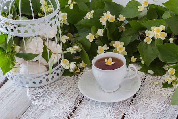 Tee mit Jasmin und Marshmallows in einem weißen dekorativen Käfig auf einem weißen Holztisch