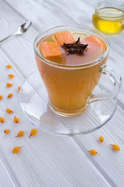 Tee mit Kürbis, Sanddorn und Gewürzen in der Glasschale auf dem weißen Holztisch.