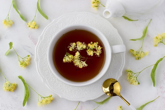 Tee mit Linde in einer weißen Tasse auf einem weißen Marmortisch Weiße Teekanne mit aromatischem Tee Draufsicht