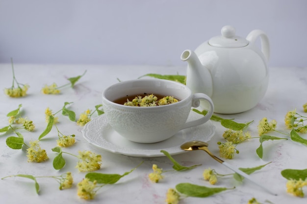 Tee mit Linden in einer weißen Tasse auf einem weißen Marmortisch Weiße Teekanne mit aromatischem Tee