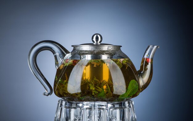 Tee mit Minze und Kräutern in einer transparenten Teekanne auf grauem Hintergrund. Isoliert mit Hintergrundbeleuchtung