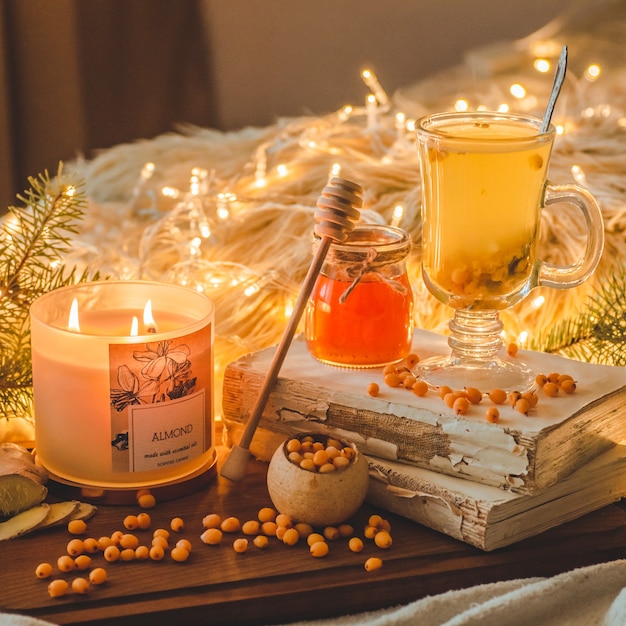 Tee mit Sanddornbeeren und Ingwer auf alten Büchern, Honig-, Kerzen- und Nadelbaumzweigen. Die Atmosphäre des Wohlbefindens zu Hause. Warmes gemütliches Zuhause.